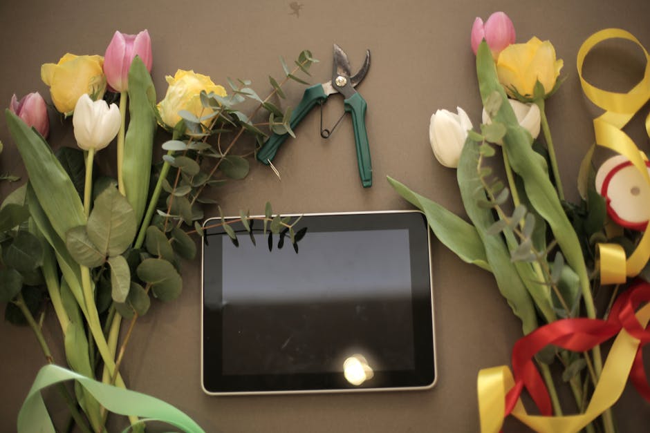 A flat lay image features an array of fresh tulips in pastel pink, yellow, and white, along with sprigs of eucalyptus leaves arranged in a semi-circle on a neutral background. The flowers are partiall