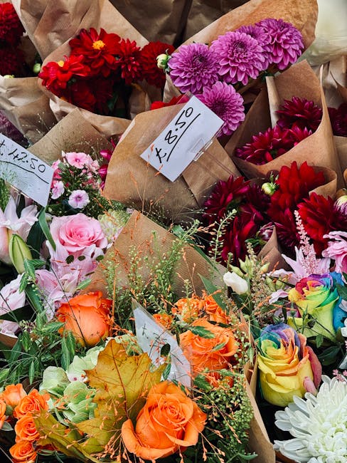 A diverse assortment of freshly prepared floral bouquets displayed at a flower market, featuring a variety of vibrant colors and flower types. Prominent among them are pink roses, orange spray roses, 