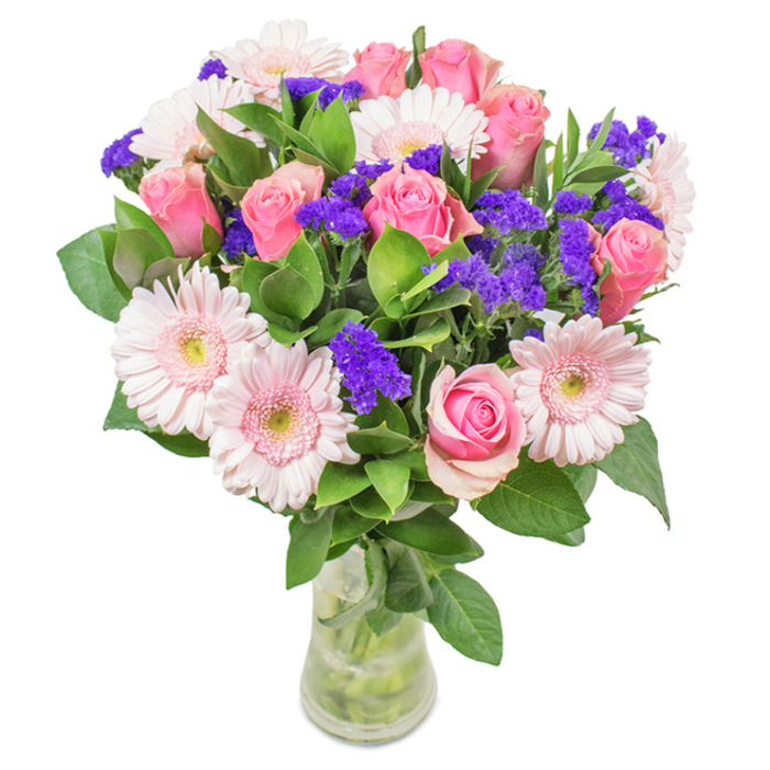 This radiant arrangement showcases the expert artistry of a Kentish Town florist, elegantly presented in a clear glass vase with visible water and stems. The bouquet features roughly 7-9 medium pink roses, each showcasing classic spirals and a velvety finish, accompanied by 5-7 pale pink Gerbera daisies whose broad faces and pale centres evoke the gardens of Rochester Place. Clusters of vivid purple statice add depth and vibrancy, their texture reminiscent of local creative spaces dotted throughout NW5. Deep green foliage spills around the edges, providing a lusciously fresh base reminiscent of morning walks through Talacre Gardens. Perfect for same-day delivery to celebrate birthdays, anniversaries, or Mother's Day-this arrangement brings to life the energy, colour, and thoughtfulness that defines Kentish Town, offering a joyful, affectionate tribute fit for home, office, or celebrations throughout the neighbourhood.